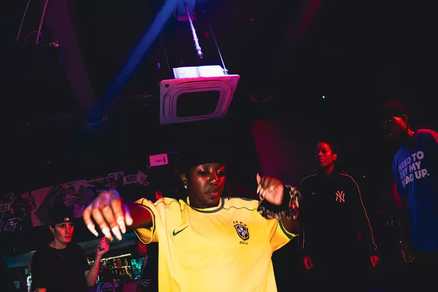 Person dancing in a dimly lit nightclub with coloruful lights while others watch in the background.