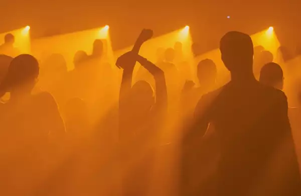 A crowd silhouetted dancing at an event bathed in orange light