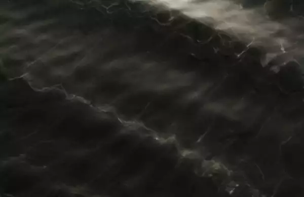 This image shows a dark, wavy surface with subtle reflections, resembling the texture of water ripples or light passing through water.
