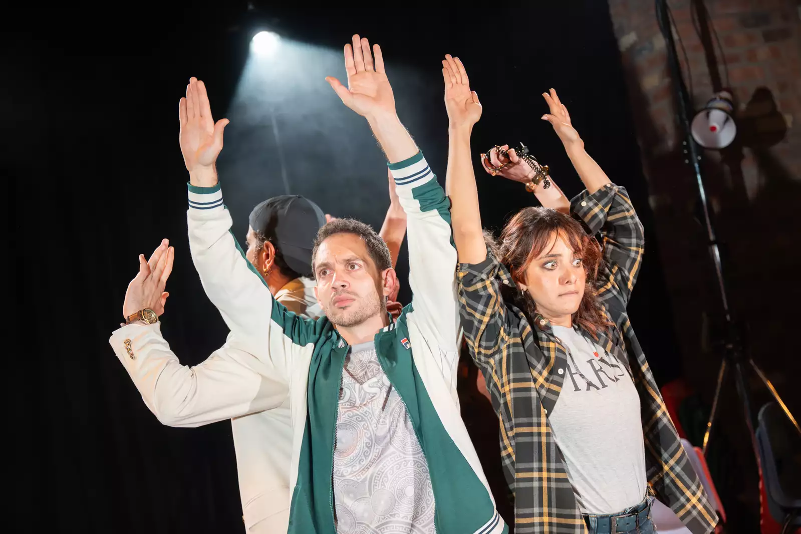 Four people on a stage hold their hands up, looking frightened.