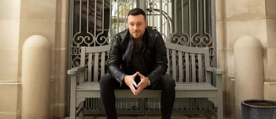 Natthan Carter sat on a bench wearing all black clothing, smiling