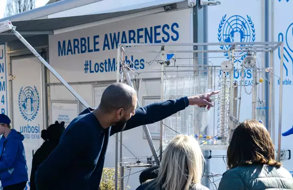 A person pointing at a marble run in front of a trailer with the words 'Marble Awareness. #LostMarbles' on