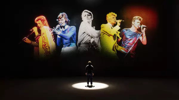 A person looking at five versions of David Bowie singing on a large screen