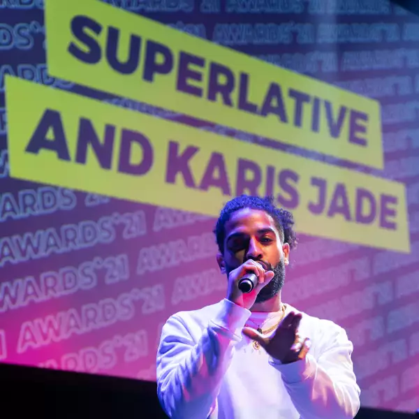 Corey Brown rapping into microphone in front of a screen that reads 'Superlative and Karis Jade'