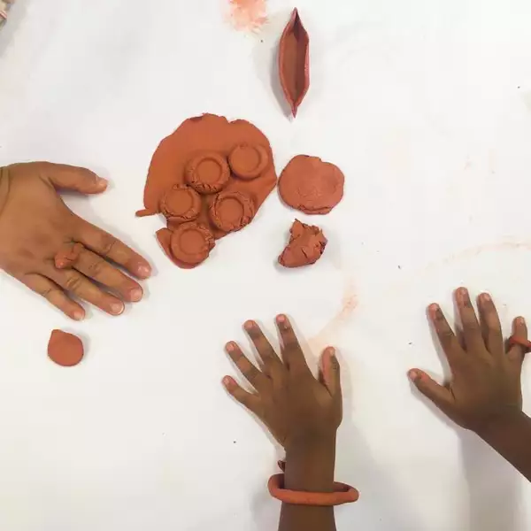 An adult and child's hands play with clay. The child has a bracelet made from clay around their wrist while the adult has a clay ring.