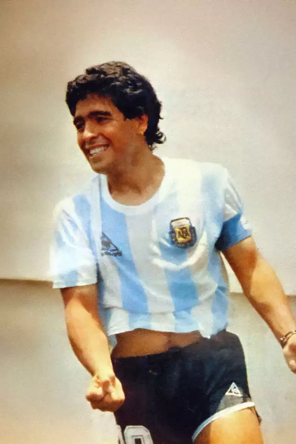 Diego Maradona wearing a football shirt, running, smiling and clenching his fist