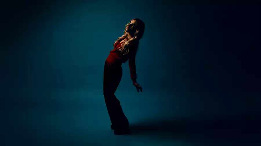 Agnes Obel standing in a blue room, bending her body and looking upwards