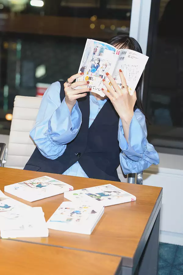 Chikyuu no Osakana Ponchan sat at a table hiding their face behind a manga book