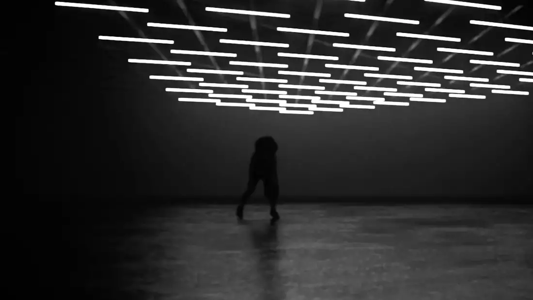 A film still that shows a figure stood beneath several bright lights