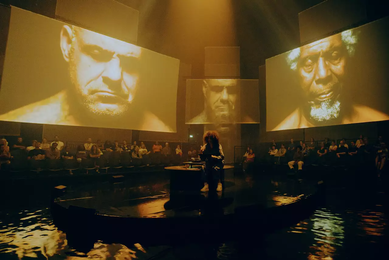 The set of A Symphony of Flesh and Bones in the Warehouse, showing projections on large screens and pieces of fabric. The screens show her brother and dad with their eyes closed.