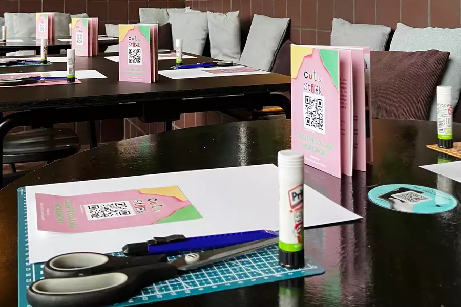 Table set up for a creative collage workshop with scissors, glue sticks, cutting mats, and colorful flyers.