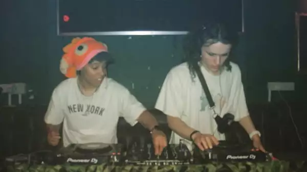 Phia and Lav behind the DJ decks, wearing white t-shirts