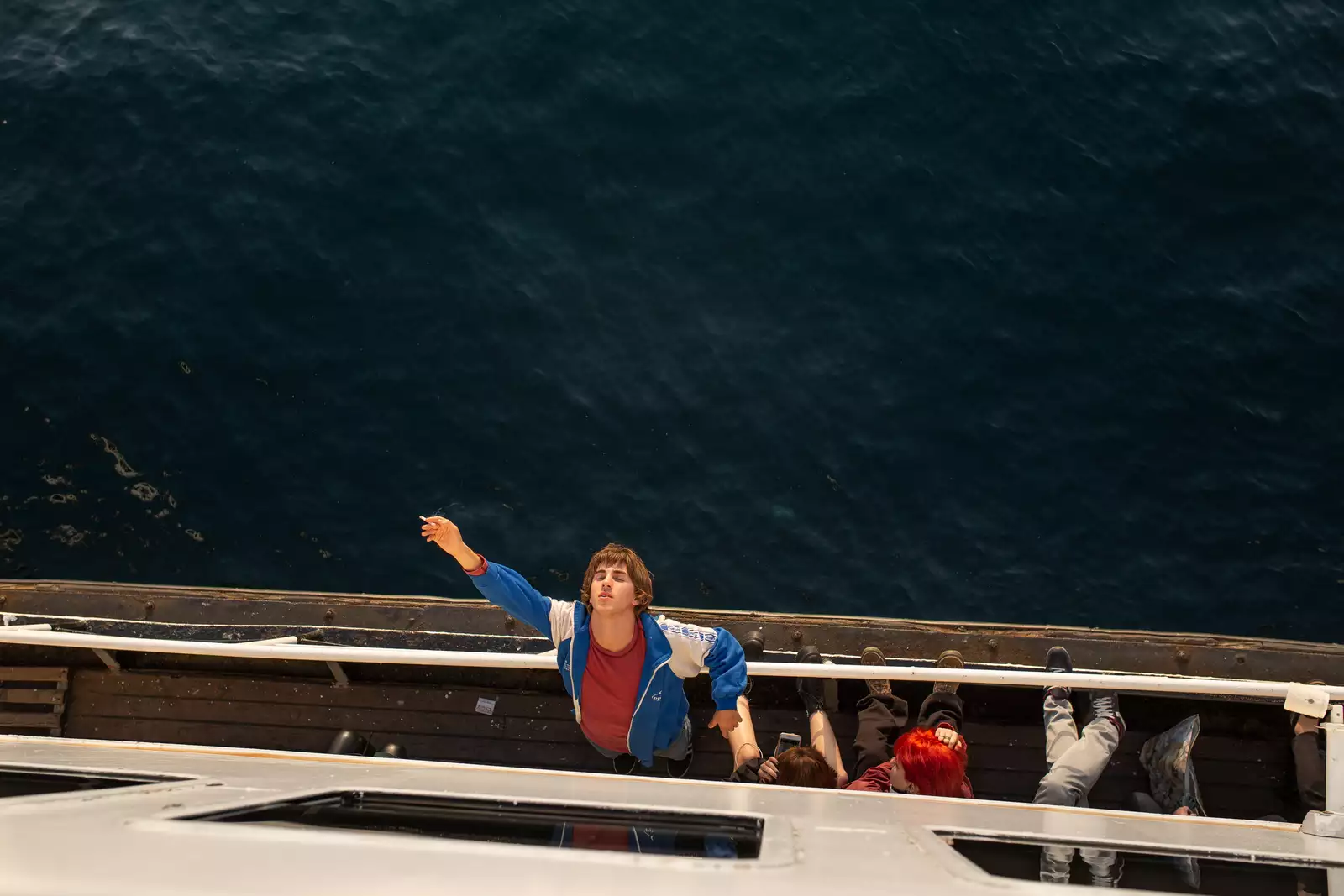 Still from Crossing. A character leaning backwards on the railings of a boat, smoking with their eyes closed. The still is taken from off.