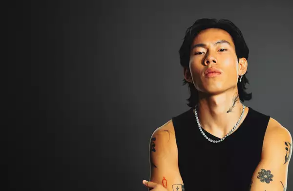 Winson wearing a black vest top and chain on a grey background