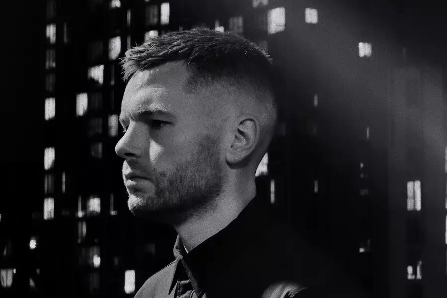 Black and white photo of Ewan Sim looking to the side. In the background is a blurry skyscraper.