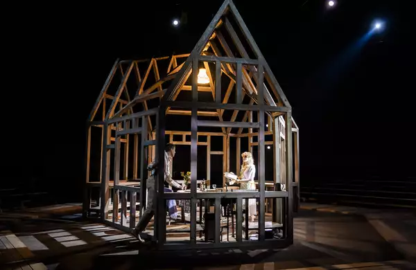 A structure of wooden beams in the shape of a house with a women standing in the middle