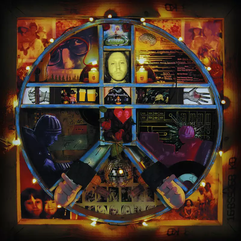 This image shows the album cover for The Hour of Bewilderbeast by Badly Drawn Boy. The cover features a circular collage of various images, photographs, and abstract designs arranged within a segmented circle. The collage includes a portrait of a person, hand-drawn elements, hands, flowers, and objects like a disco ball. The color scheme is a mix of deep reds, blues, and yellows, giving the design a warm, nostalgic, and eclectic feel. Lights surround the outer edge of the circle, adding a glowing effect.