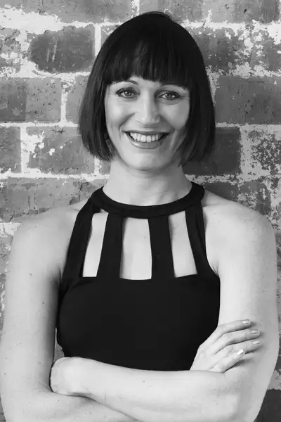 Black and white headshot of Elise May stood against a brick wall