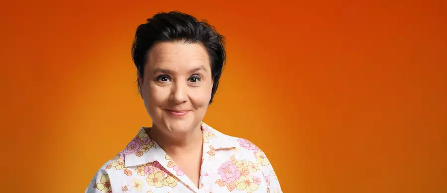 Susan Calman smiling and wearing a flowery shirt on a bright orange background