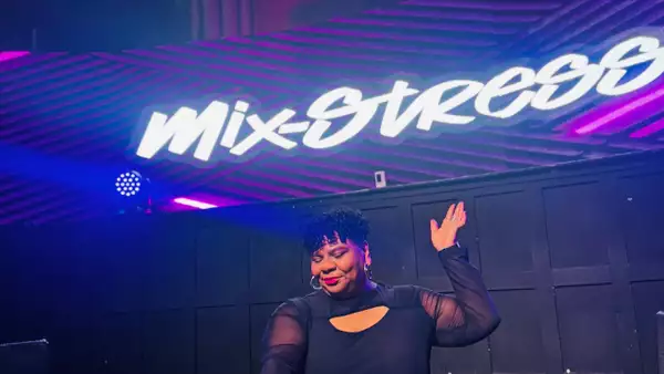 Mix-Stress DJing and smiling under a sign which reads 'Mix-Stress' with purple lighting