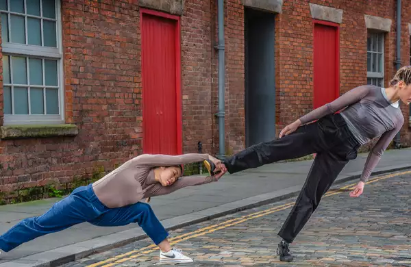 Two people holding a balancing position outdoors on a cobbled street