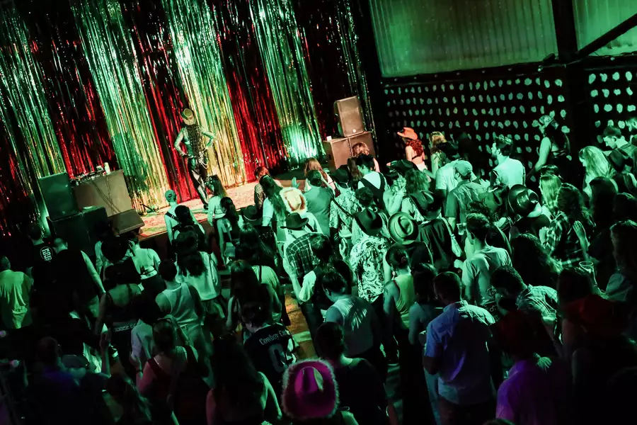 A large crowd of people line-dancing. Shanika Sunrise is on stage guiding the crowd, in front of a glittery curtain.