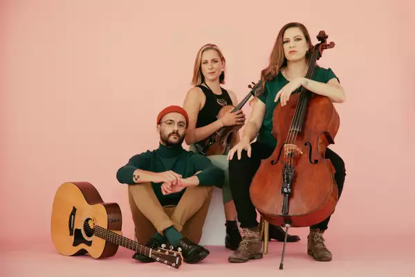 Three members of É.T.É with their instruments, on a light pink background