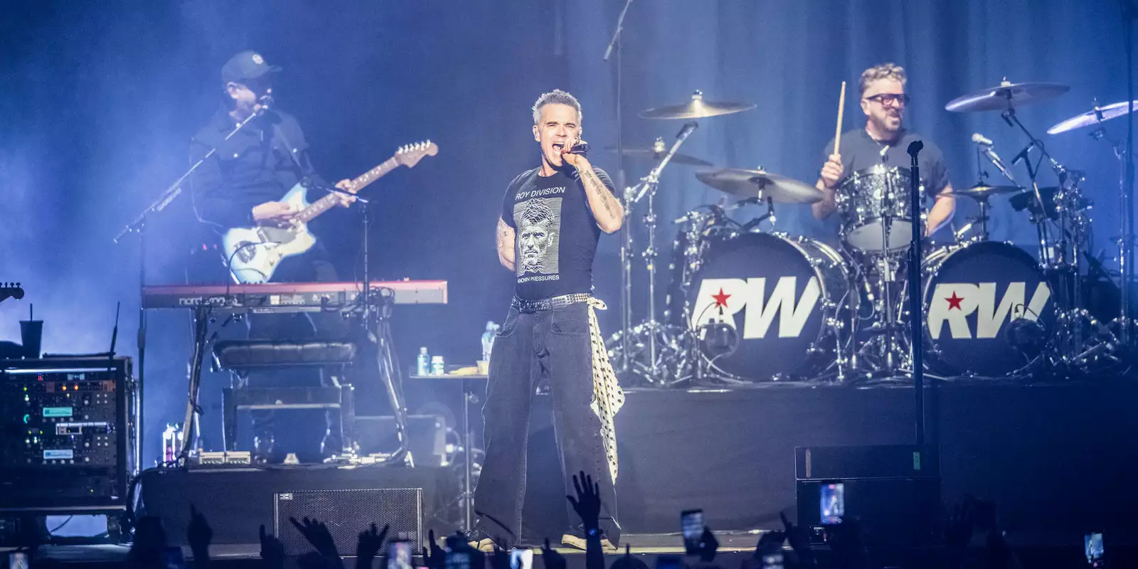 Robbie Williams on stage at Aviva Studios singing and playing guitar