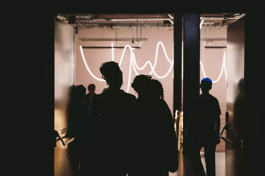 The outlines of people walking into the dark Warehouse – with bright lights in the stairway