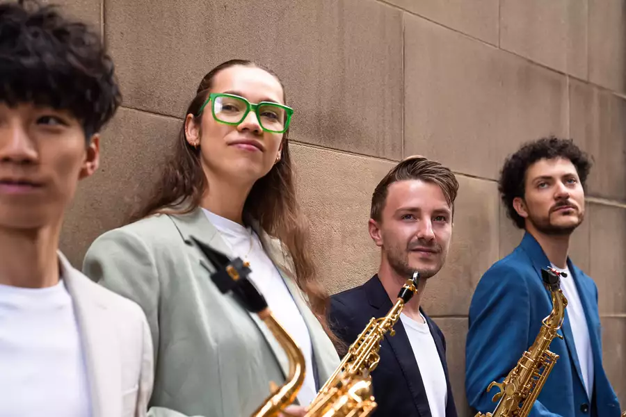 The Fractal Saxophone Quarter stand side on with saxophones looking into the camera in front of a brick wall