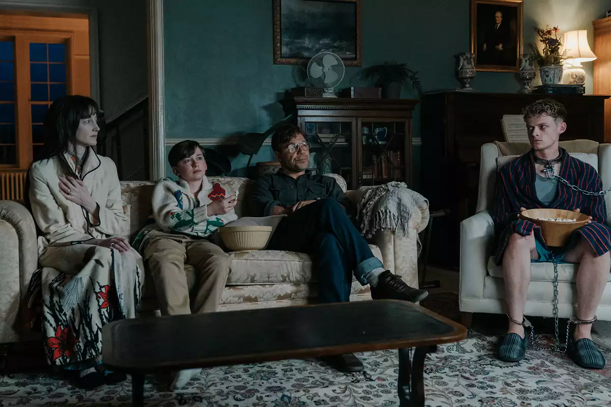 Still from The Good Boy showing a family sat on a sofa in a living room, with one man in chains