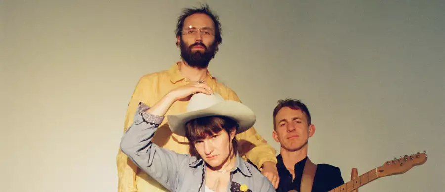 Three members of Big Thief on a white background. Adrianne Lenker is wearing a white cowboy hat.
