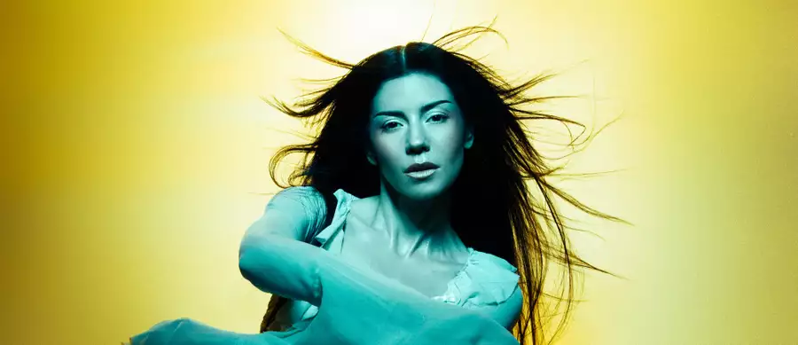 MARINA with long flowing hair poses against a yellow background