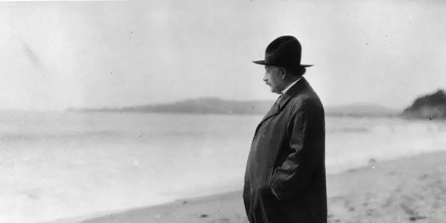 An archive image of Albert Einstein standing on a beach looking out towards the sea.