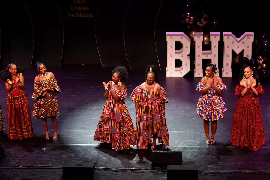 A group of people stood on stage clapping and smiling at Black Creative Trailblazers. Behind them are big letters spelling 'BHM' for Black History Month. They are wearing colourful African dress.