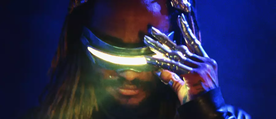 Thundercat wearing futuristic glowing visor glasses and metallic claw-like gloves against a dark blue background.