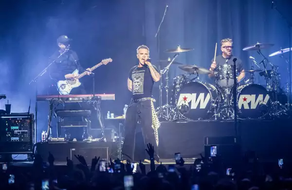 Robbie Williams on stage at Aviva Studios singing and playing guitar