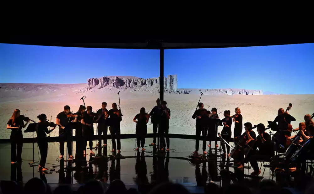 Manchester Collective performing in front of two huge screens, which show imagery of a desert