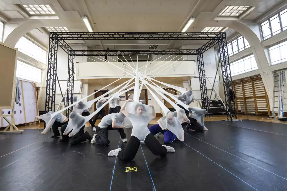 Dancers in stretched white fabric attached to a rig in rehearsals for Free Your Mind