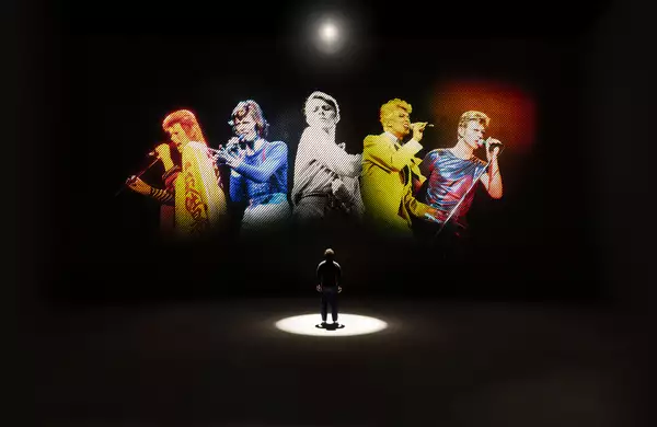 A person looking at five versions of David Bowie singing on a large screen