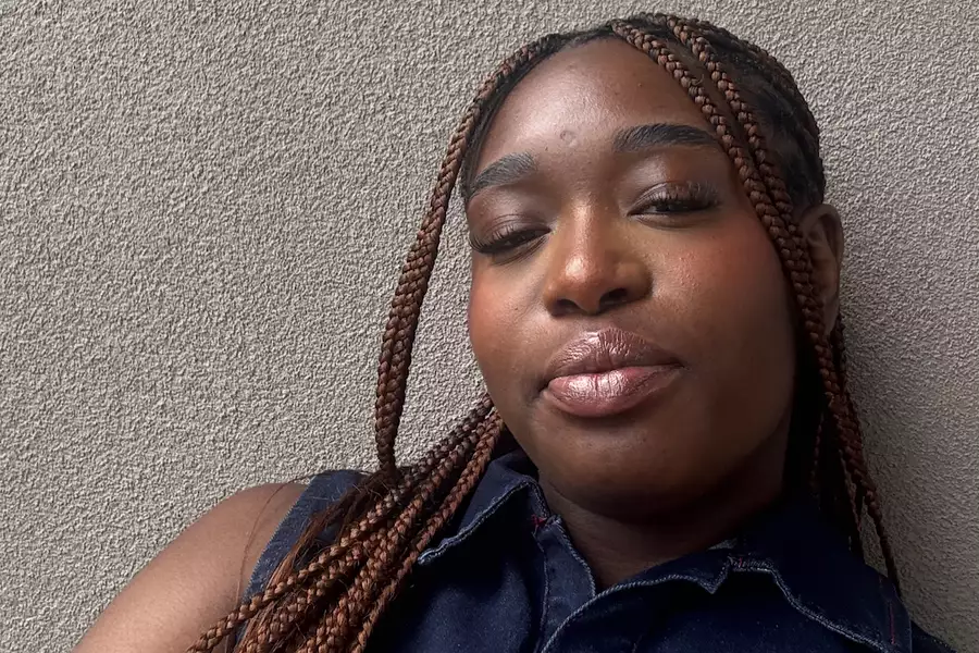 Adele Tondu wearing a denim top leaning against a grey wall