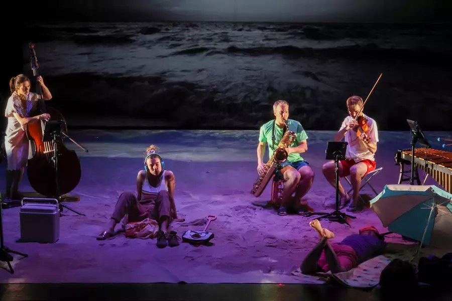 A scene of performance from All Right Good Night, actors sat on a beach setting