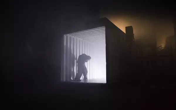 A photo of a dark warehouse space and a person stood silhouetted against a bright light coming from a shipping container