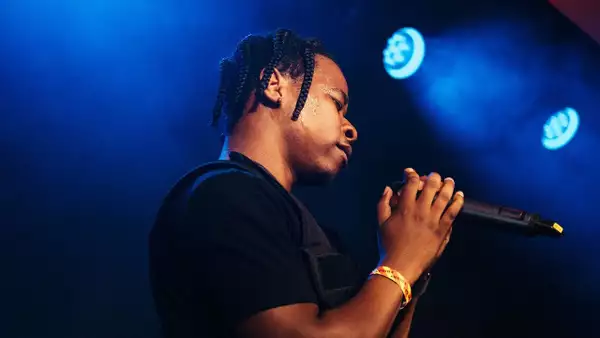 PRIDO singing into a microphone on Festival Square. The lighting is blue.