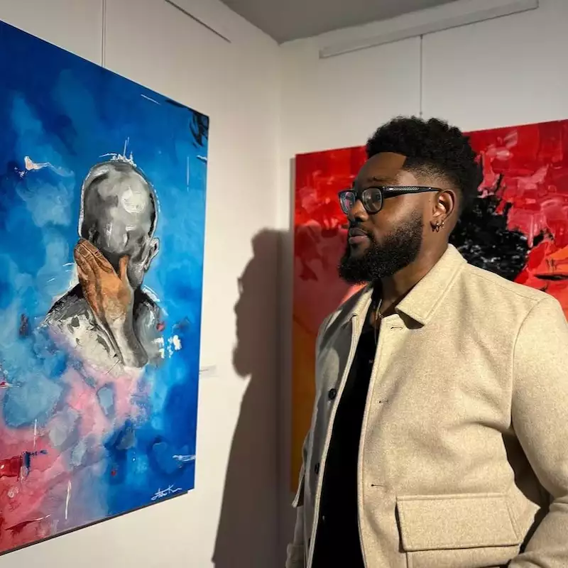 Andrew Kuwornu wearing a beige jacket, looking at a brightly coloured painting