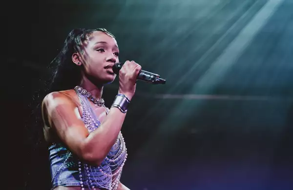 A performer on stage singing into a microphone and wearing a beaded top