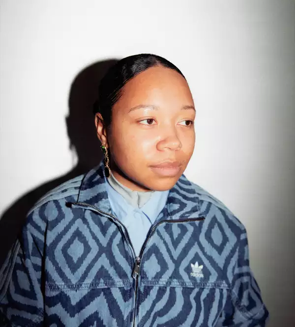 Kymara Akinpelumi wearing a patterned denim Adidas jacket on a white background