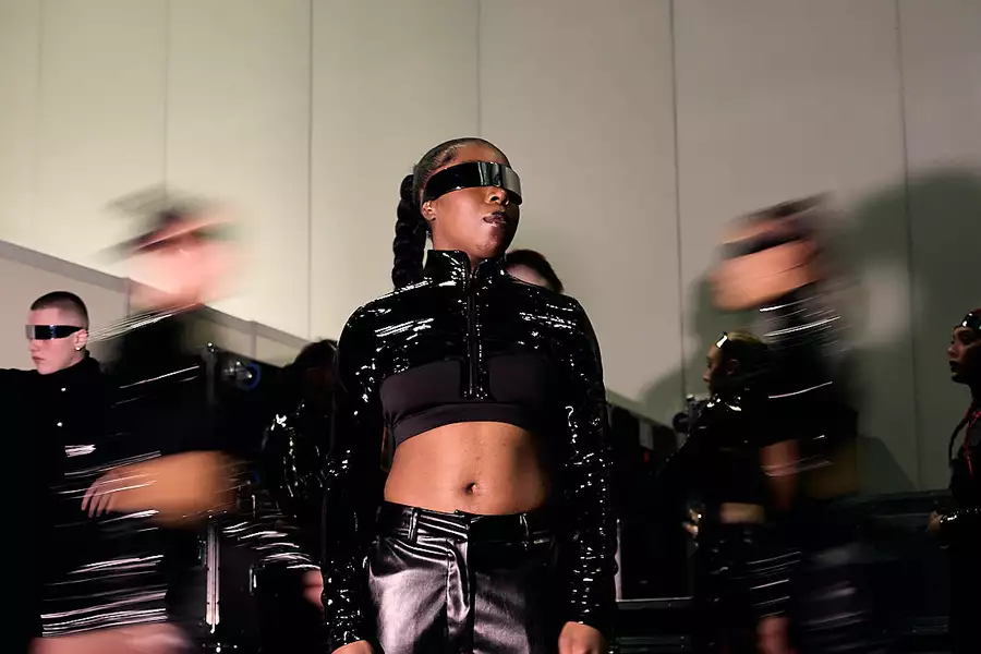 A dancer wearing black leather and a band across their eyes. Behind them are blurry outlines of other dancers.