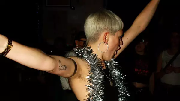 A person dancing with their hands in the air, with silver tinsel around their neck.