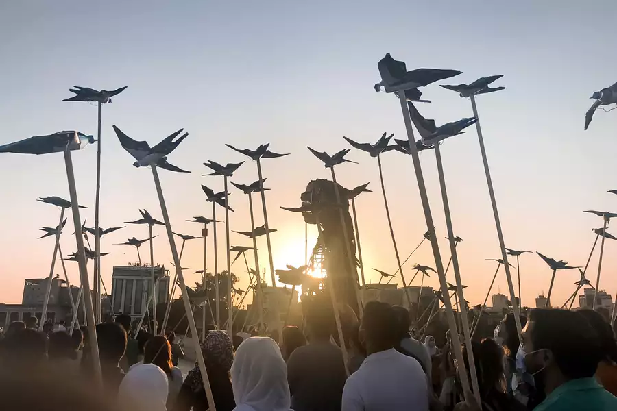 Against the setting sun, the 3.5-metre tall Little Amal puppet walks alongside a crowd of people holding up birds on sticks, fashioned out of water bottles